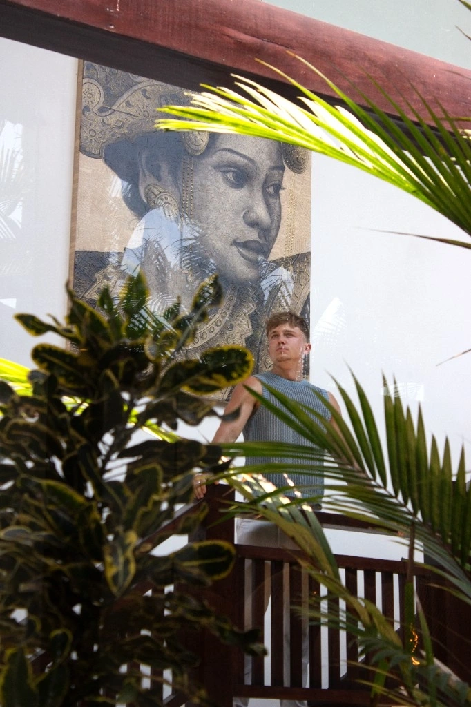 Lukas on a wooden balcony with tropical plants and artwork