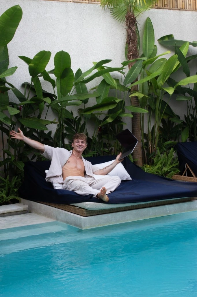 Lukas relaxing by the pool with a laptop on a daybed